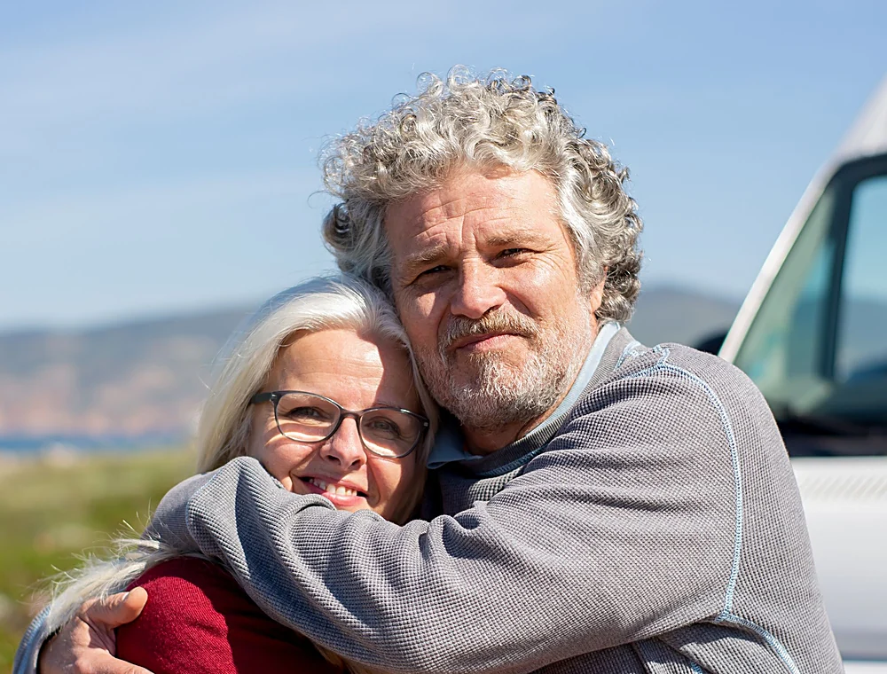 A couple in their sixties hugging outdoors on a sunny day