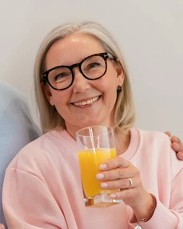 A woman in her sixties smiling at home with a glass of fresh juice &mdash; Welavie supplement reviews