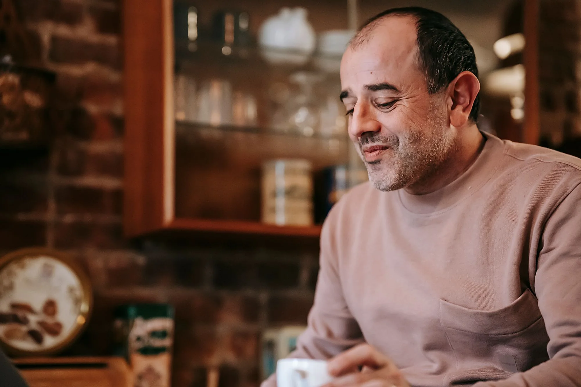 A man smiling down at his morning coffee in a warm kitchen