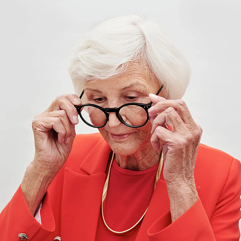 A woman in her seventies adjusting her glasses to look at something up close