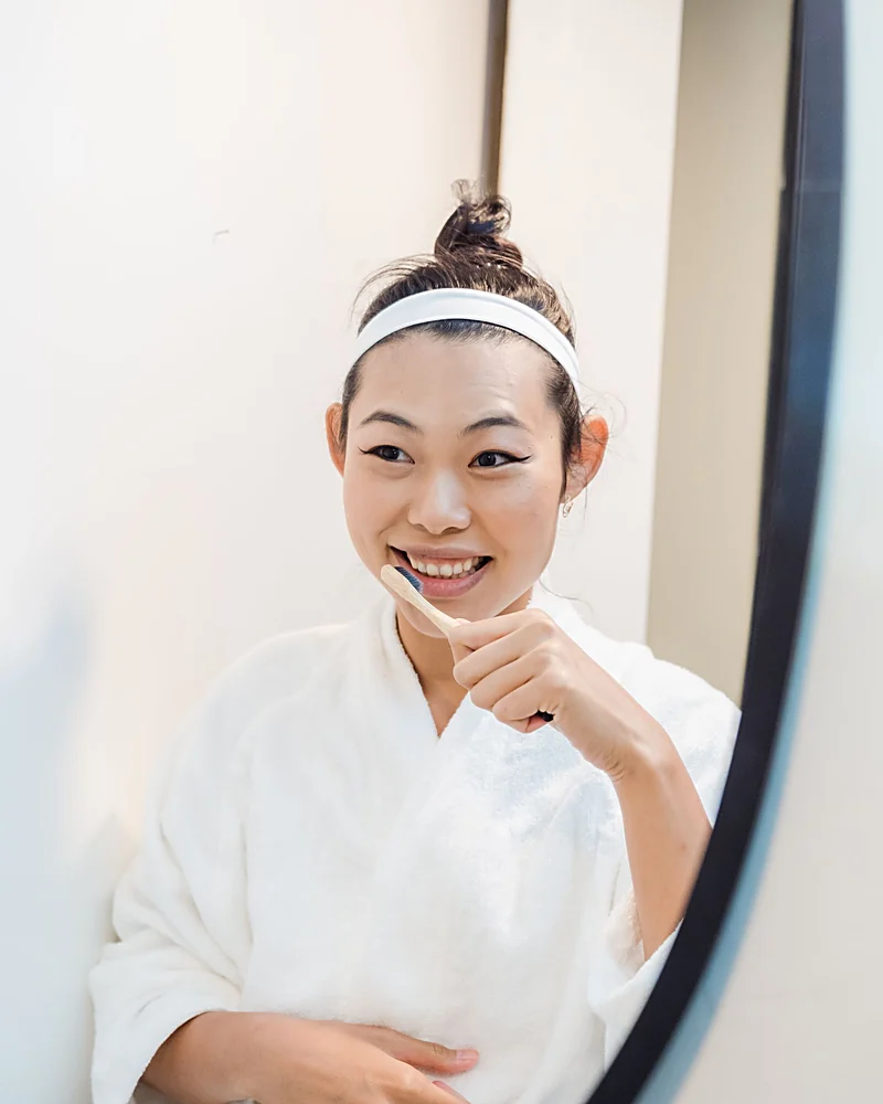 A woman in a bathrobe smiling into the bathroom mirror during her morning routine