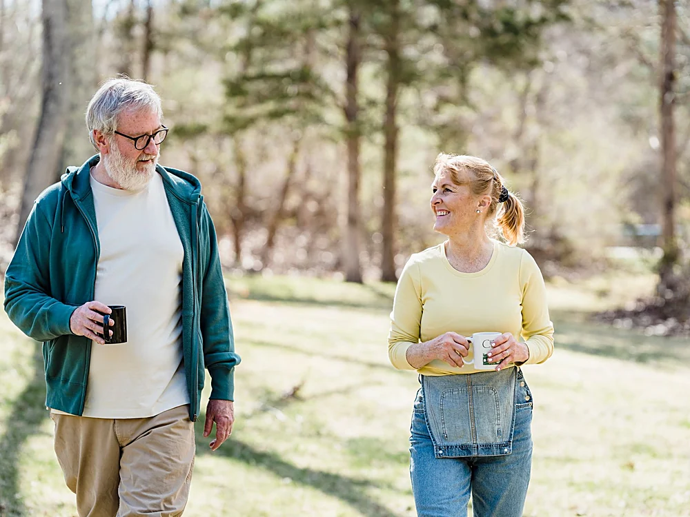 A couple walking through a park with mugs of coffee