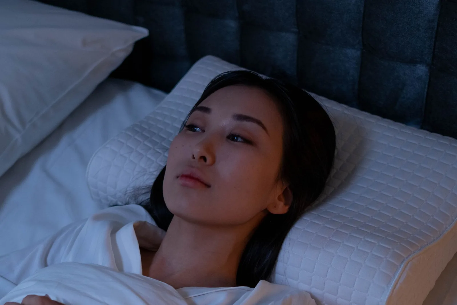 A woman lying awake in a dark bedroom in the small hours, staring at the ceiling